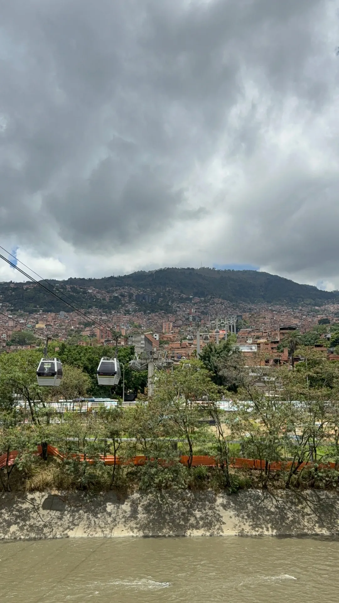 Metrocable gondolas crossing above the river with the hillside city behind